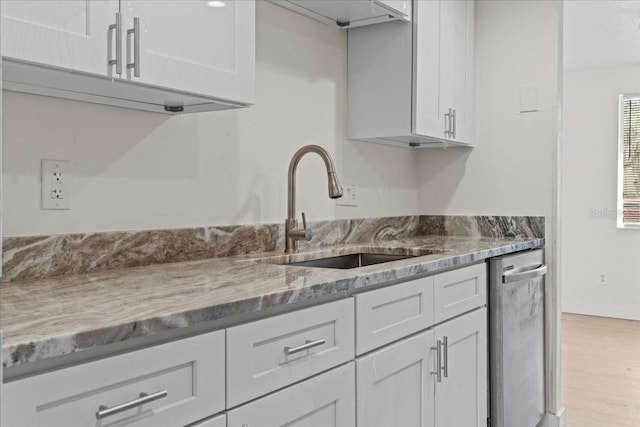 kitchen featuring sink, white cabinetry, stainless steel dishwasher, light stone countertops, and light hardwood / wood-style floors