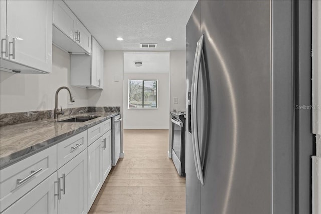 kitchen featuring sink, stainless steel appliances, white cabinets, dark stone counters, and light wood-type flooring