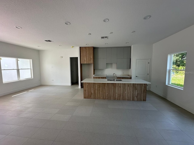 kitchen featuring light tile patterned floors, sink, a textured ceiling, and an island with sink