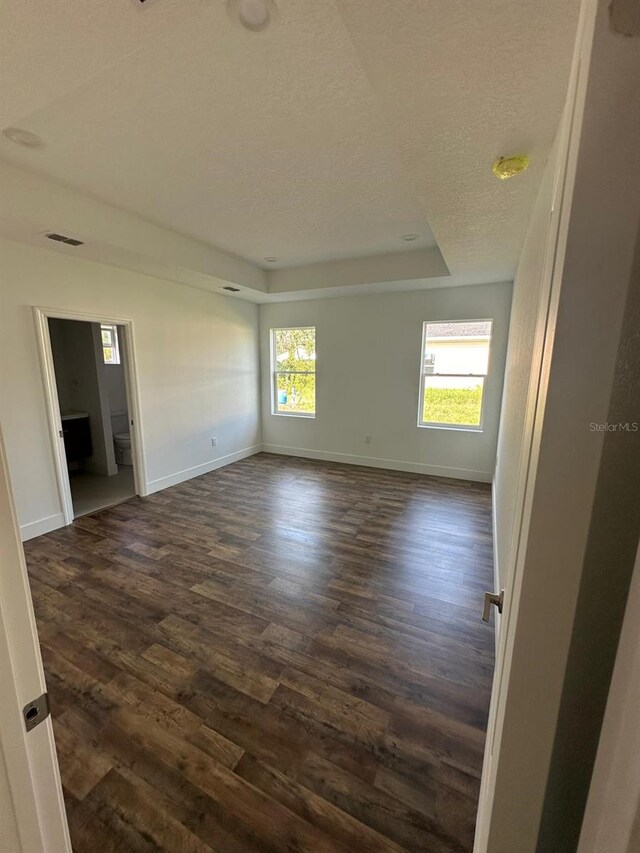 unfurnished room with dark hardwood / wood-style flooring, a raised ceiling, and a textured ceiling