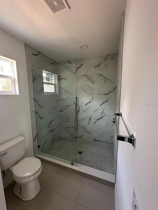 bathroom with a textured ceiling, toilet, a shower with shower door, and tile patterned floors