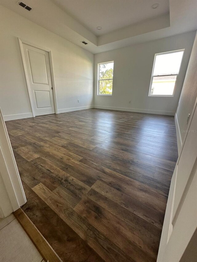 empty room with a raised ceiling and dark wood-type flooring