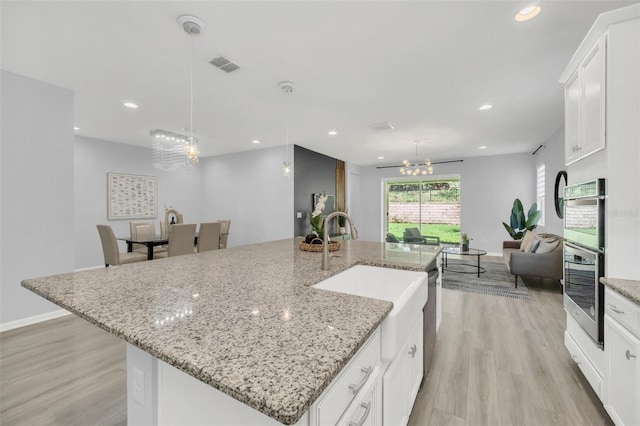 kitchen with light hardwood / wood-style floors, a center island with sink, and white cabinetry