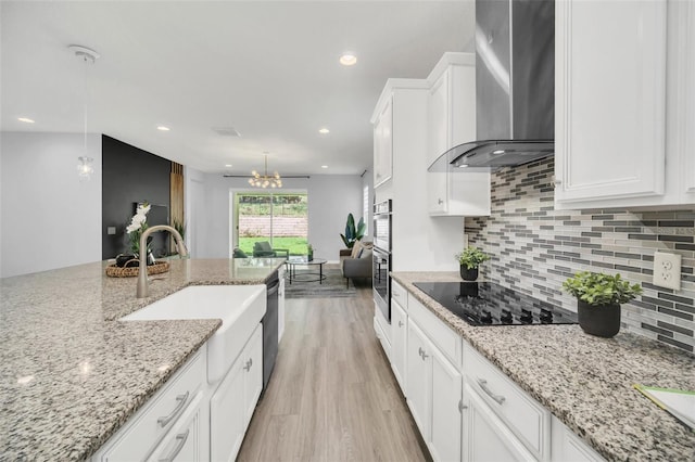 kitchen with light wood-type flooring, black electric stovetop, white cabinetry, light stone counters, and wall chimney range hood