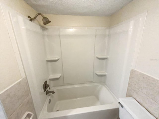 bathroom featuring toilet, washtub / shower combination, and a textured ceiling