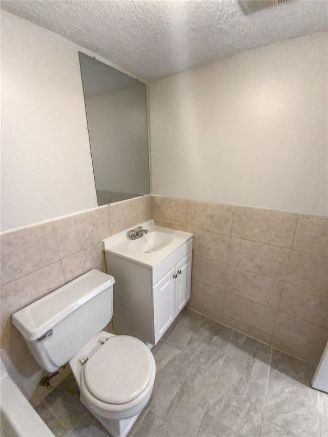 bathroom with vanity, tile flooring, a textured ceiling, and tile walls