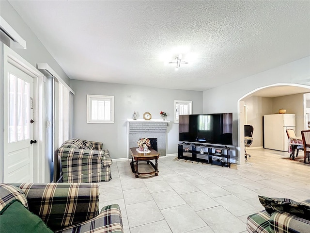 tiled living room with a textured ceiling and a brick fireplace