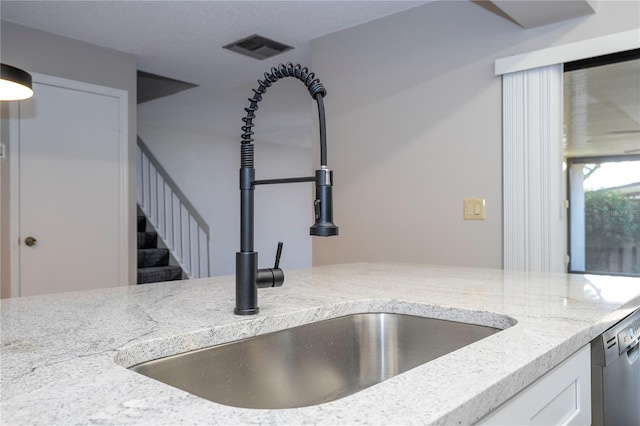 room details featuring dishwasher, sink, light stone countertops, and white cabinets