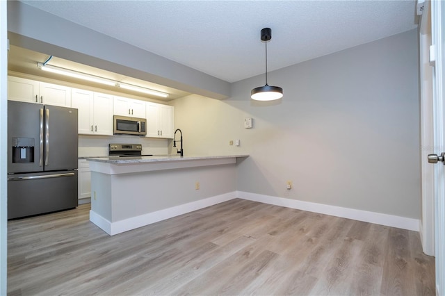 kitchen with appliances with stainless steel finishes, kitchen peninsula, white cabinets, and pendant lighting