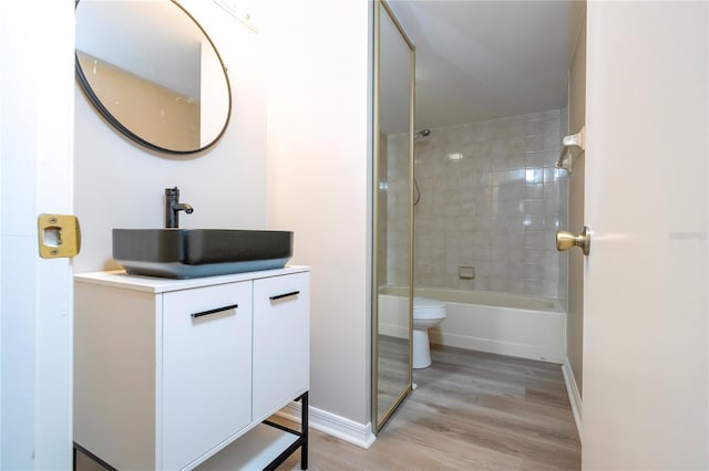 full bathroom featuring hardwood / wood-style floors, toilet, tiled shower / bath combo, and vanity