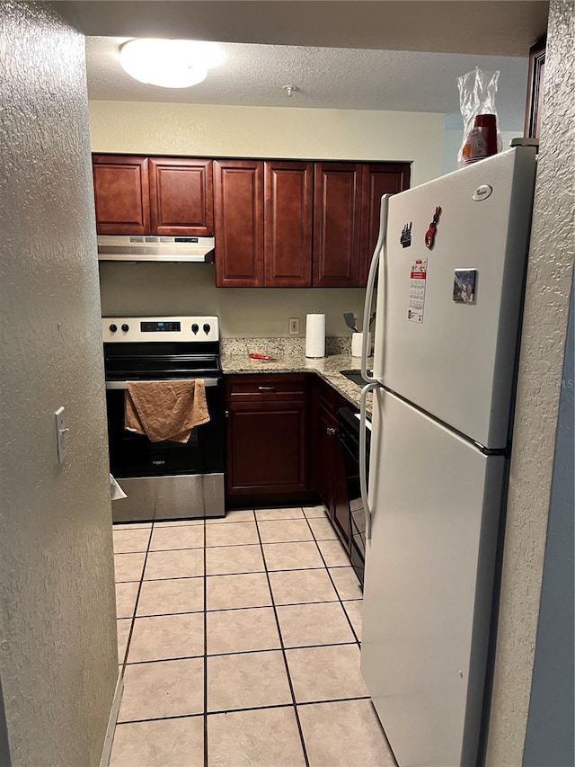 kitchen featuring light tile floors, range, white fridge, and light stone countertops