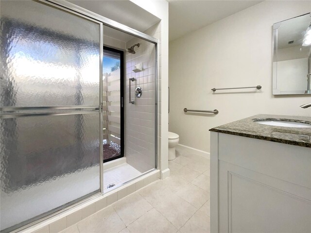 bathroom featuring tile patterned flooring, vanity, toilet, and a shower with shower door