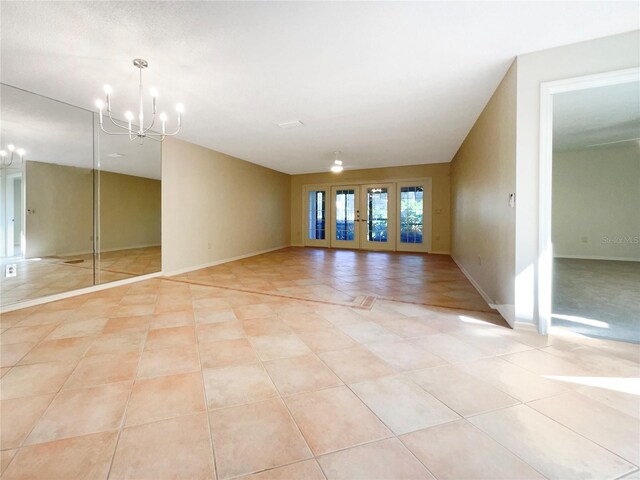 empty room with light tile patterned flooring, an inviting chandelier, and french doors