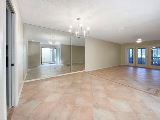 empty room featuring a textured ceiling, french doors, light tile patterned flooring, and a notable chandelier