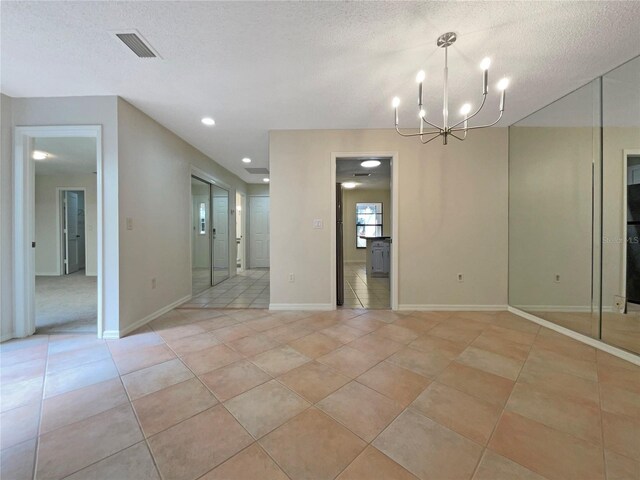 spare room featuring light tile patterned flooring, a chandelier, and a textured ceiling