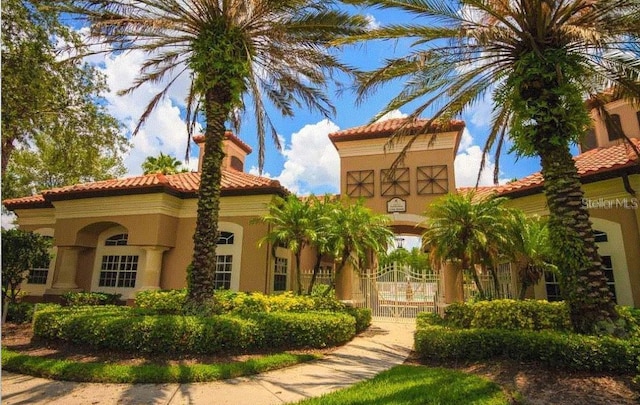 mediterranean / spanish house featuring a tiled roof, a gate, and stucco siding