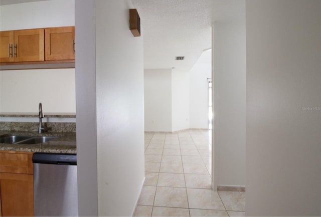 kitchen with dark stone countertops, dishwasher, light tile patterned flooring, and sink