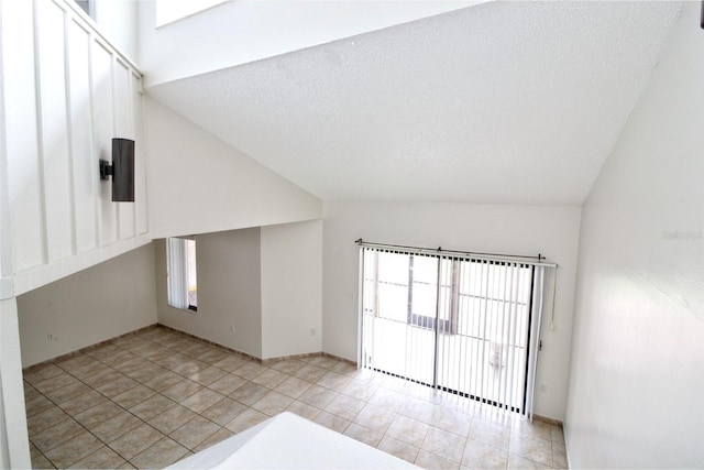 tiled spare room featuring a wealth of natural light, vaulted ceiling, and a textured ceiling