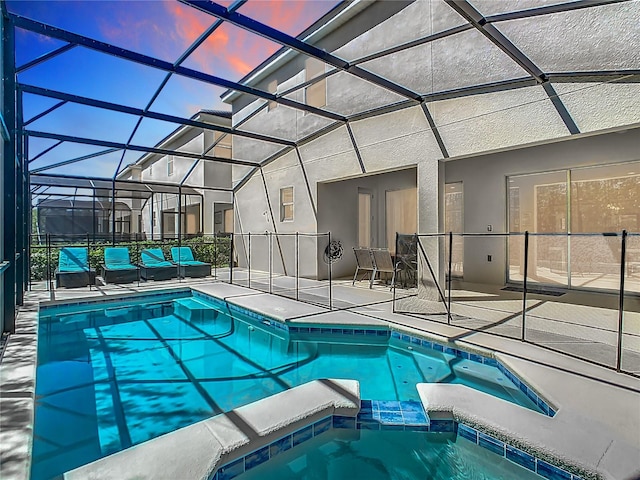 pool at dusk featuring a patio, an in ground hot tub, and a lanai