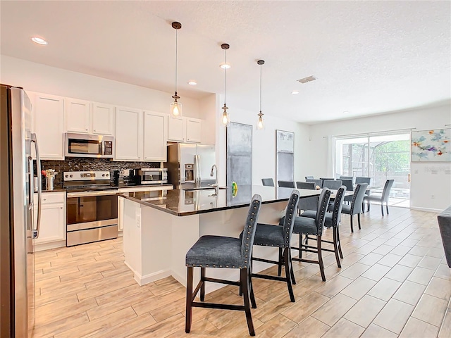 kitchen featuring an island with sink, pendant lighting, a kitchen breakfast bar, and appliances with stainless steel finishes