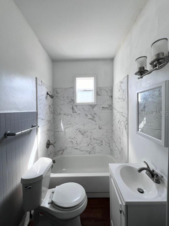 full bathroom with toilet, tiled shower / bath combo, vanity, and wood-type flooring