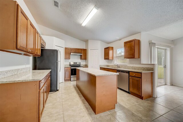 kitchen featuring stainless steel appliances, a textured ceiling, light stone counters, a center island, and light tile floors