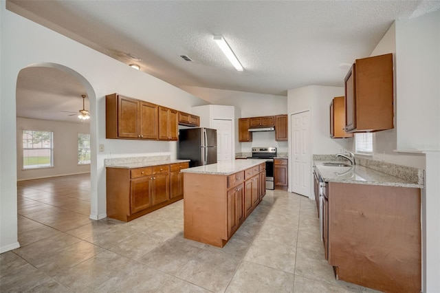 kitchen with a kitchen island, ceiling fan, stainless steel appliances, light stone counters, and light tile floors