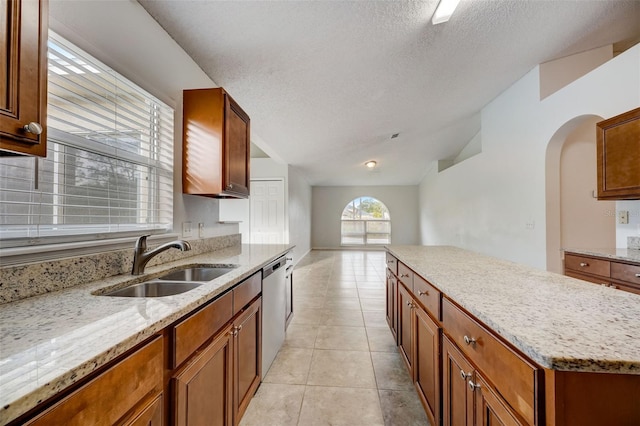 kitchen with light stone countertops, light tile flooring, stainless steel dishwasher, sink, and a textured ceiling