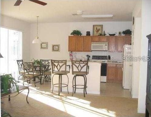 kitchen featuring decorative light fixtures, ceiling fan, a kitchen breakfast bar, and white appliances