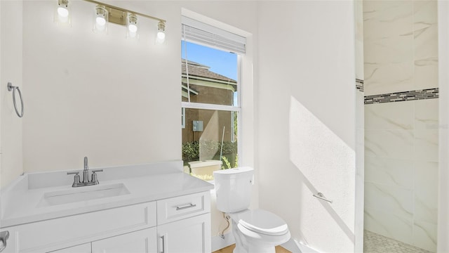 bathroom with a tile shower, vanity, and toilet