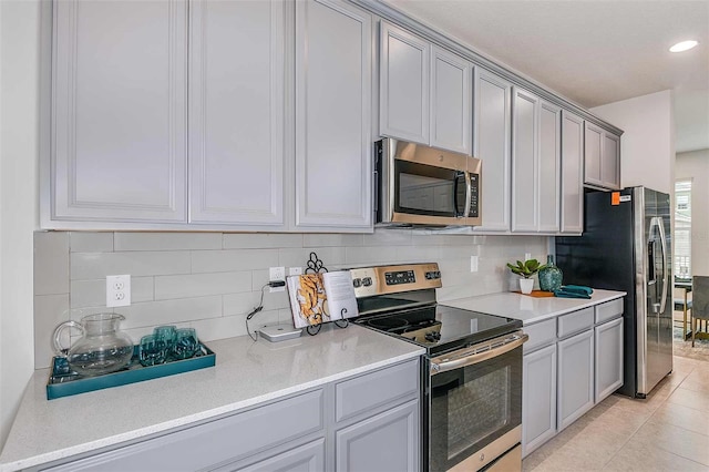 kitchen with gray cabinets, light tile patterned floors, backsplash, and appliances with stainless steel finishes