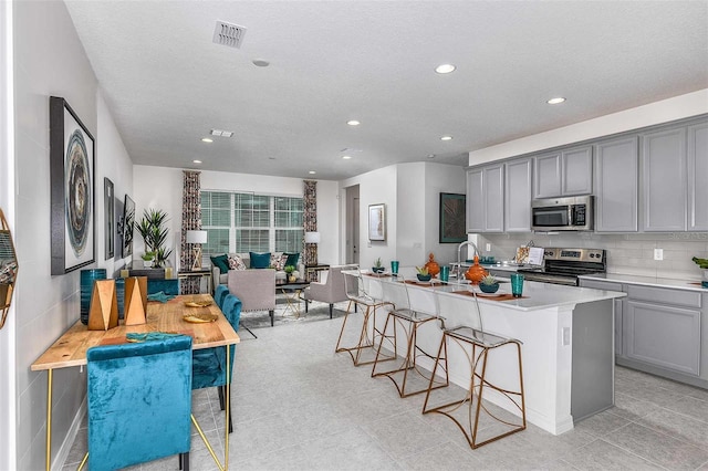 kitchen with gray cabinetry, a kitchen island with sink, decorative backsplash, and appliances with stainless steel finishes