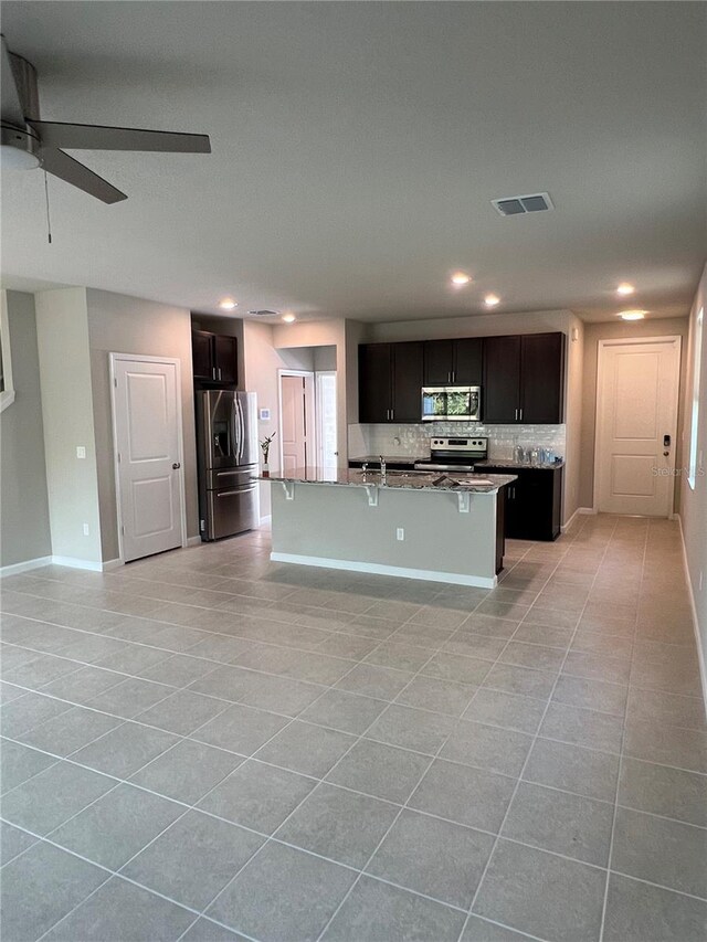 kitchen with a kitchen island with sink, a breakfast bar, visible vents, appliances with stainless steel finishes, and backsplash