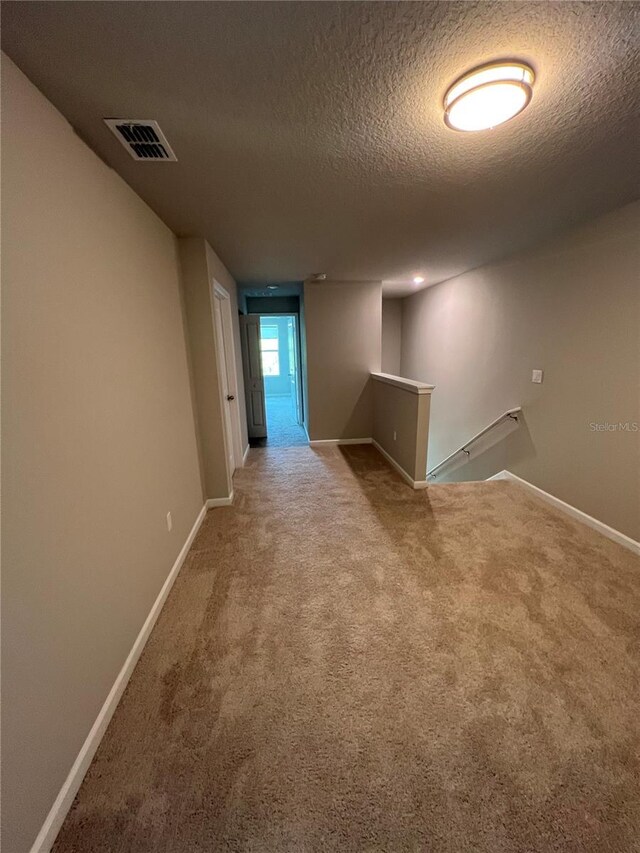 unfurnished room featuring carpet, visible vents, a textured ceiling, and baseboards