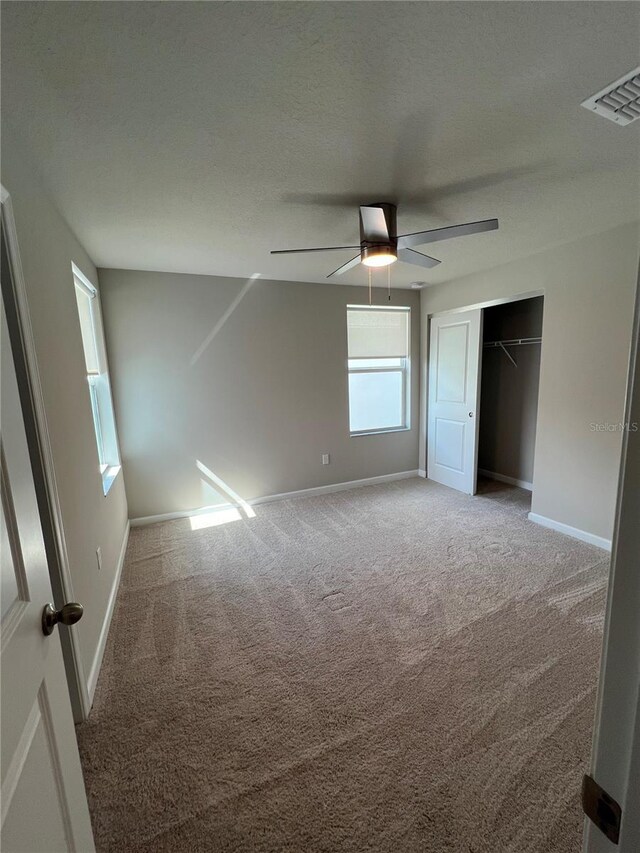 unfurnished bedroom with a textured ceiling, carpet flooring, a ceiling fan, baseboards, and a closet