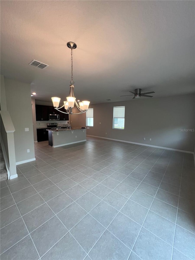 unfurnished living room with light tile patterned floors, baseboards, visible vents, stairs, and ceiling fan with notable chandelier