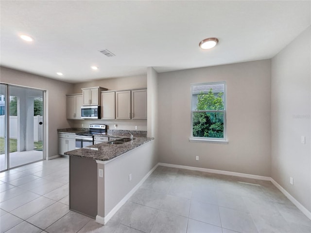 kitchen featuring kitchen peninsula, light tile flooring, sink, stainless steel appliances, and dark stone countertops