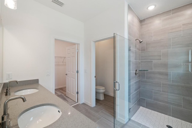 bathroom with a shower with door, toilet, tile floors, and dual vanity