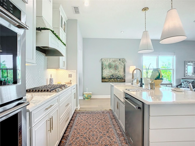 kitchen with stainless steel appliances, a kitchen island with sink, hanging light fixtures, and white cabinetry