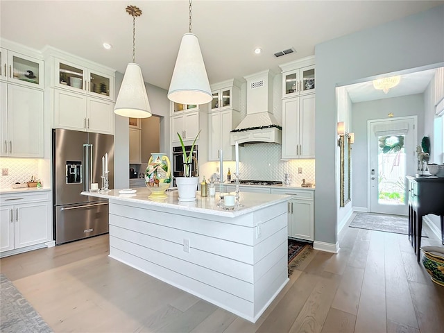 kitchen featuring stainless steel appliances, an island with sink, custom range hood, and hanging light fixtures