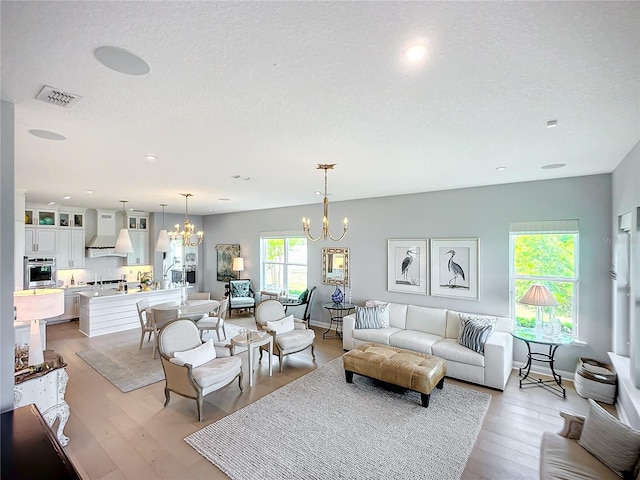 living room featuring a textured ceiling, a notable chandelier, and light hardwood / wood-style floors