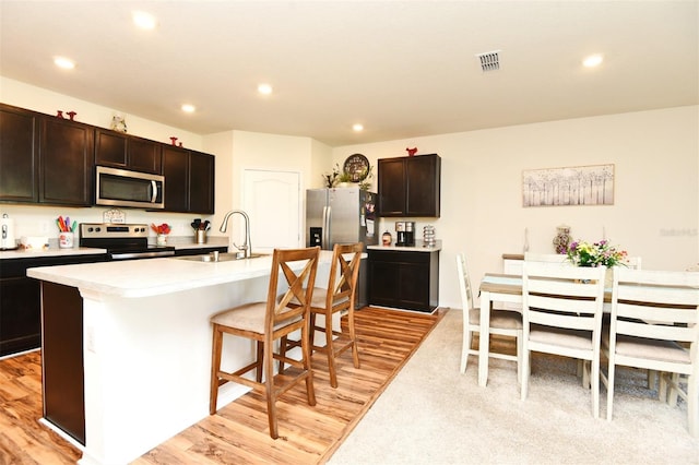 kitchen with appliances with stainless steel finishes, a kitchen bar, sink, an island with sink, and dark brown cabinetry