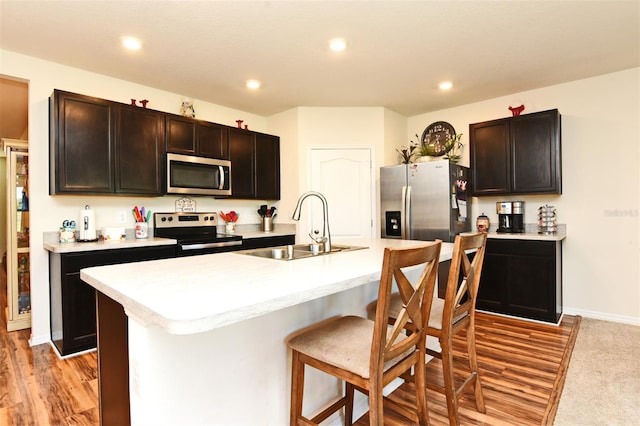 kitchen featuring a kitchen island with sink, sink, stainless steel appliances, light carpet, and dark brown cabinetry