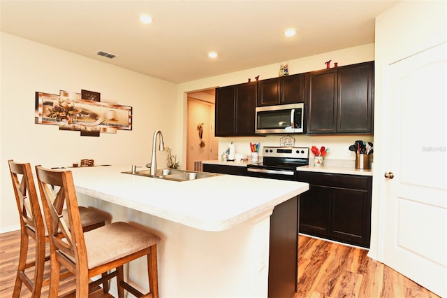 kitchen featuring a kitchen breakfast bar, appliances with stainless steel finishes, light hardwood / wood-style floors, sink, and a center island with sink