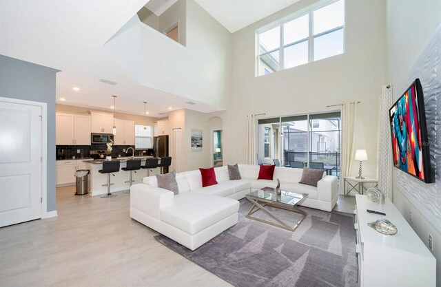 living room with light hardwood / wood-style floors, a high ceiling, sink, and a wealth of natural light