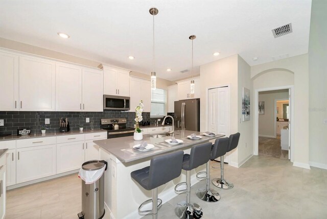 kitchen featuring light tile floors, decorative light fixtures, appliances with stainless steel finishes, white cabinetry, and a kitchen island with sink