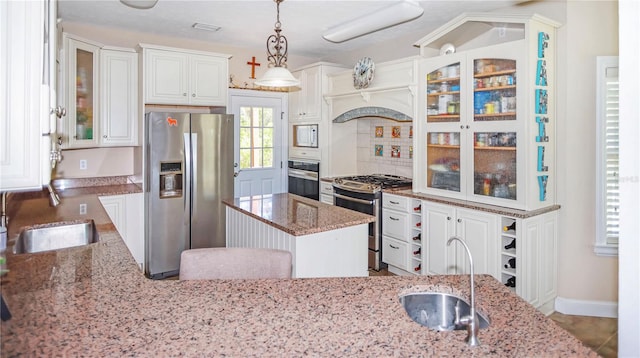 kitchen with appliances with stainless steel finishes, light stone counters, sink, pendant lighting, and a center island