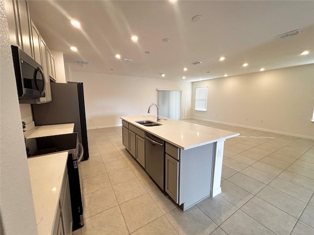 kitchen with stainless steel appliances, sink, a center island with sink, and light tile patterned floors