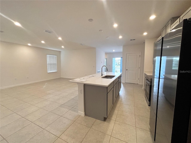 kitchen with sink, light tile patterned floors, stainless steel fridge, a kitchen island with sink, and stove