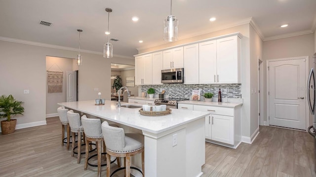 kitchen with sink, hanging light fixtures, stainless steel appliances, white cabinets, and a center island with sink